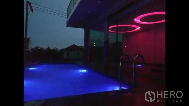 Detached House for sale in Lat Phrao, Bangkok - Night view of illuminated swimming pool and colorful LED ceiling lights.