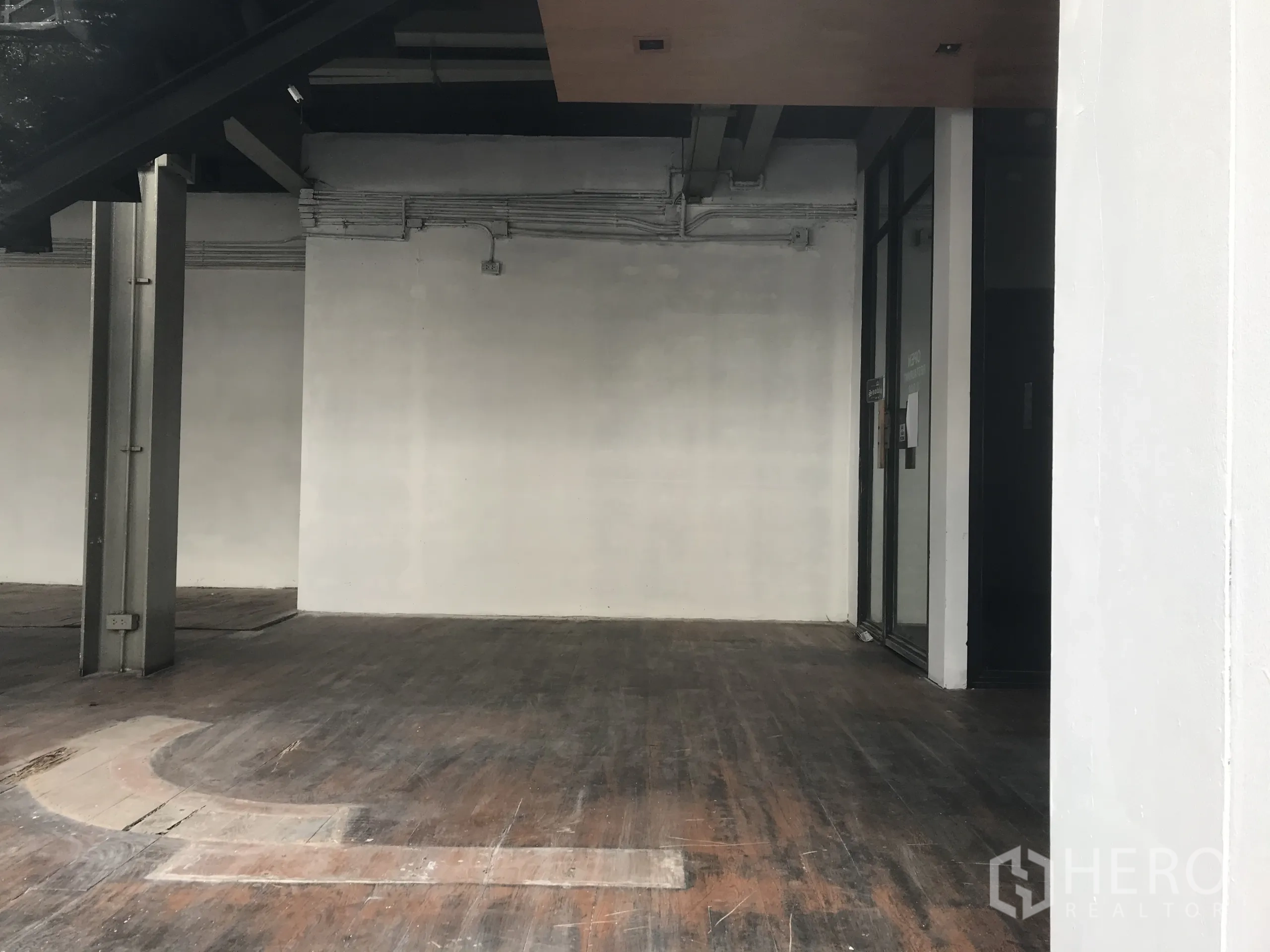 Retail Space for rent in Watthana, Bangkok - Empty retail space with white walls, exposed services, dark wooden flooring, and a rear access door.