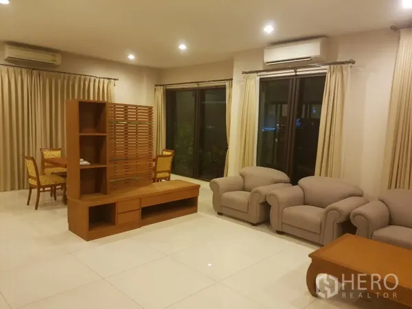 Townhouse for rent in Bang Kapi, Bangkok - Spacious living room with tiled floors, beige sofas, wooden media unit and sliding glass doors.