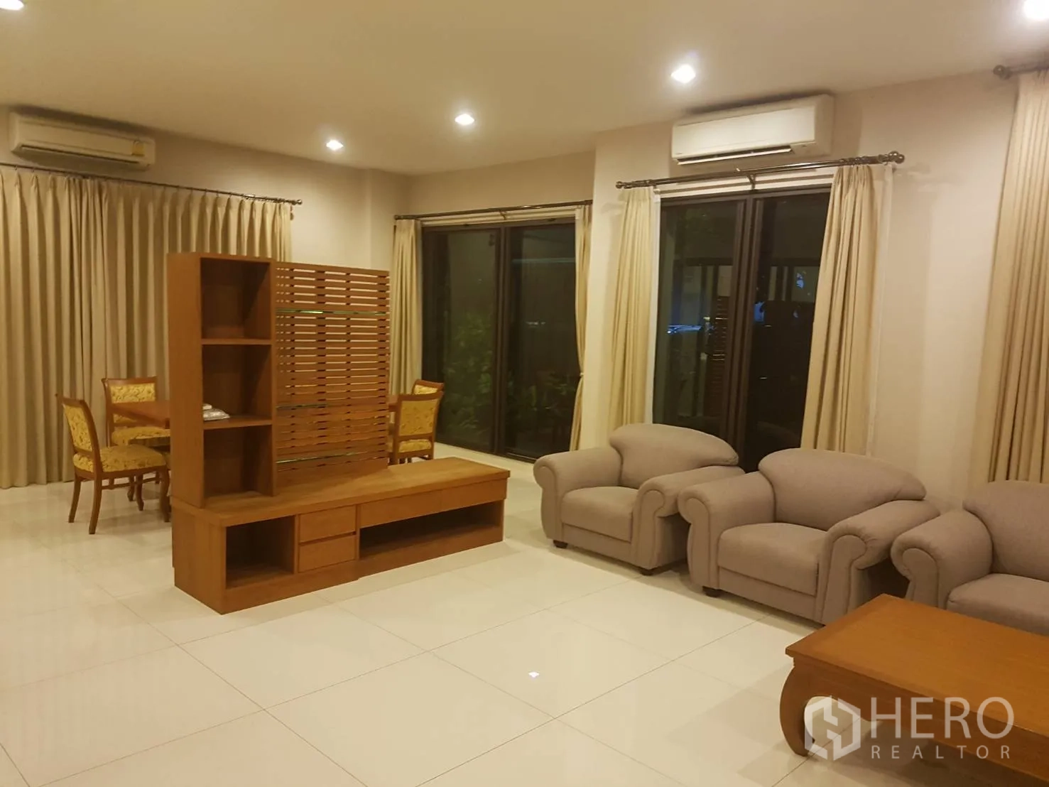 Townhouse for rent in Bang Kapi, Bangkok - Spacious living room with tiled floors, beige sofas, wooden media unit and sliding glass doors.
