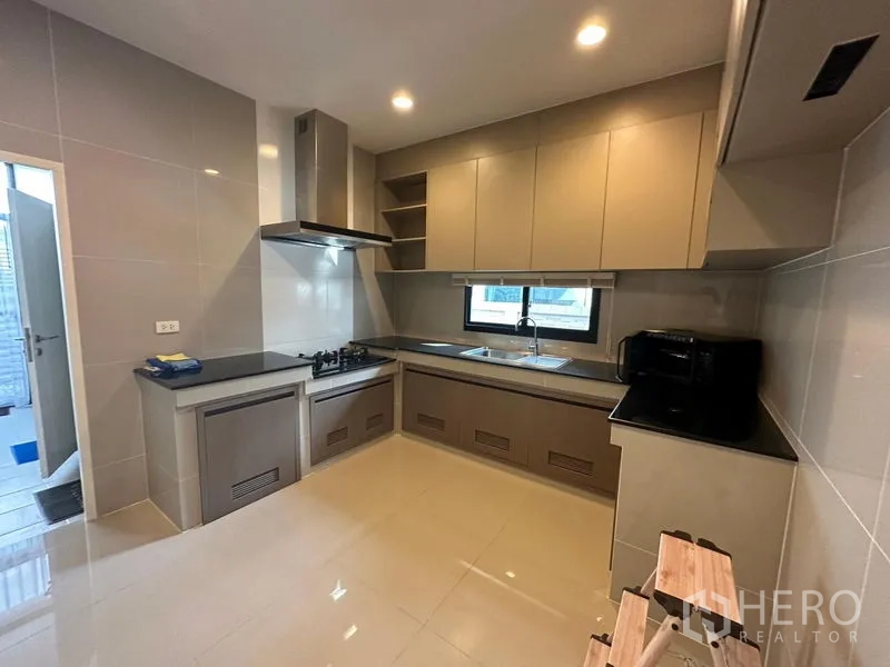 Detached House for rent or sale in Lam Luk Ka, Pathum Thani - Built-in kitchen with L-shaped counters, gas hob, range hood, window and ample cabinets.