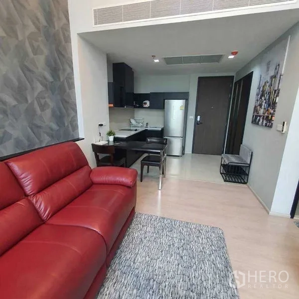 Condominium for rent in Khlong Toei, Bangkok - Cozy lounge with a red leather sofa, area rug and view toward the open-plan kitchen and dining area.