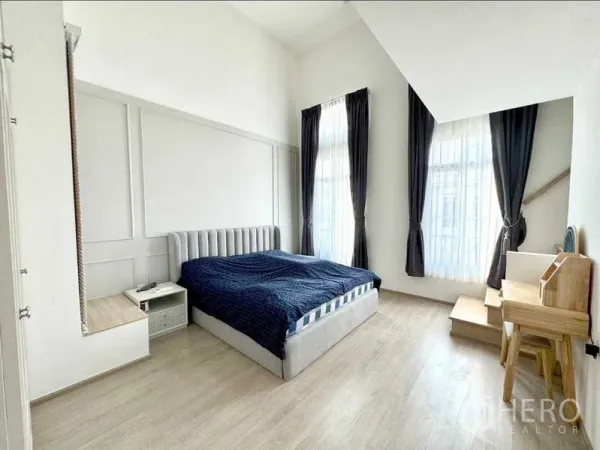 Townhouse for rent or sale in Prawet, Bangkok - Master bedroom with high ceiling, tall windows, light wood floors and a built‑in desk.
