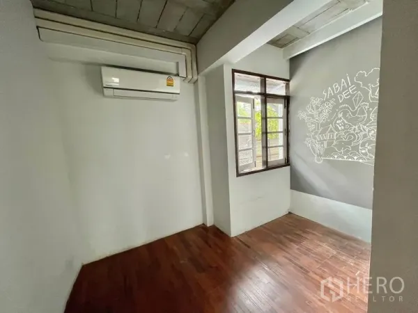 Shophouse for rent in Pathum Wan, Bangkok - Compact room with wooden floor, opening window, air conditioner and a decorative mural.