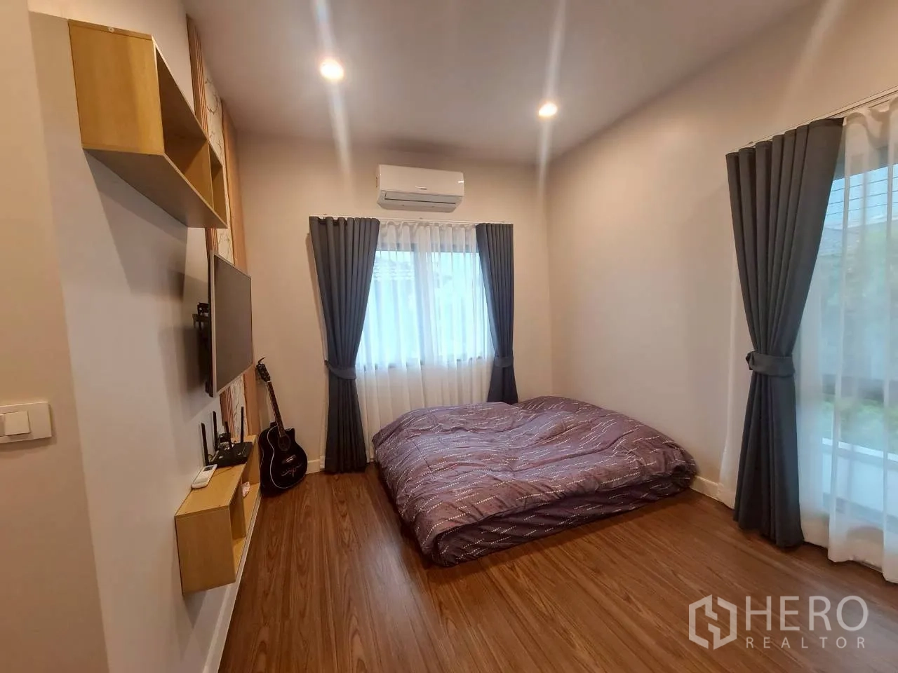 Detached House for rent or sale in Lam Luk Ka, Pathum Thani - Third bedroom with floor bed, two windows, wall-mounted TV and guitar.