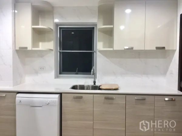 Condominium for rent in Pathum Wan, Bangkok - Bright kitchen wall with sink, window, glossy cabinets and an integrated dishwasher.