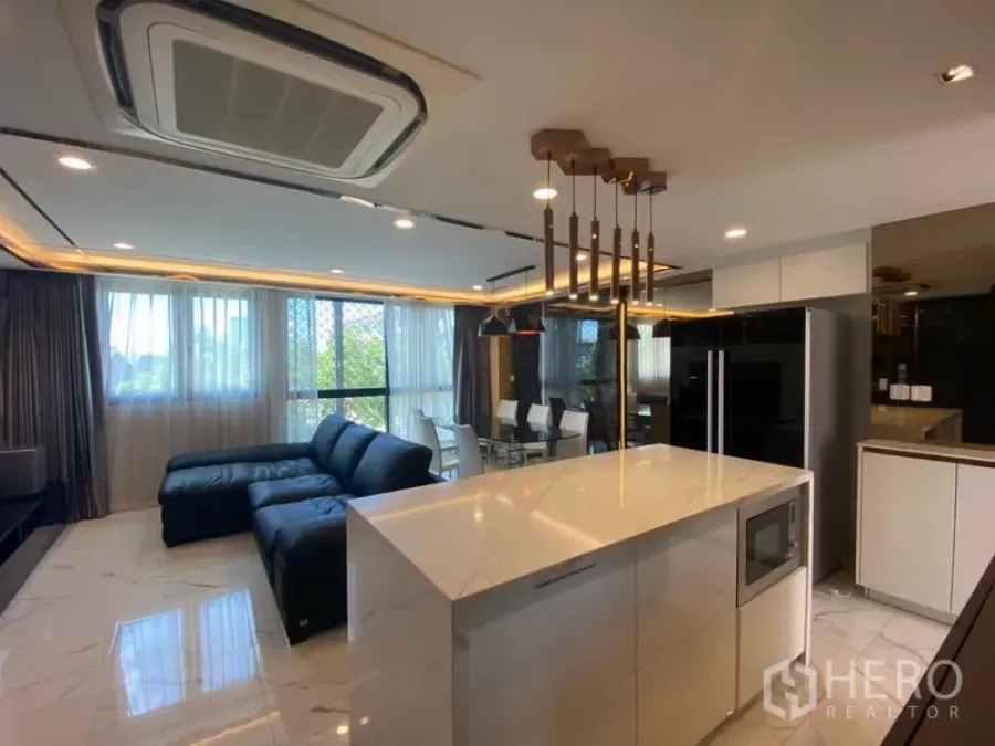 Townhouse for sale in Yan Nawa, Bangkok - Open‑plan living area with marble floors, a black sectional sofa and a sleek island kitchen under pendant lights and large windows.