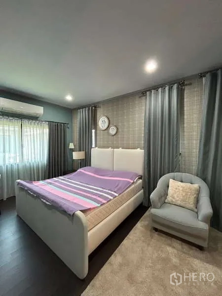 Detached House for rent in Bang Kapi, Bangkok - Bright bedroom with white upholstered bed, armchair, and gray drapes.