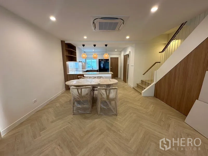 Home Office for rent in Khlong Toei, Bangkok - Dining zone beside the staircase leading to a modern kitchen with island and pendant lights.
