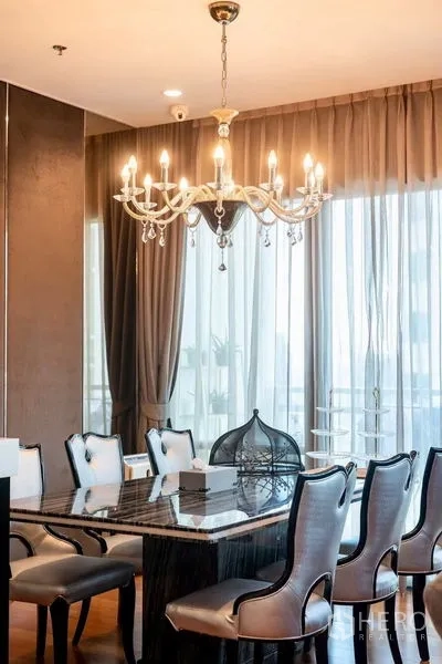 Condominium for rent in Khlong Toei, Bangkok - Formal dining area with marble table and crystal chandelier by large windows.