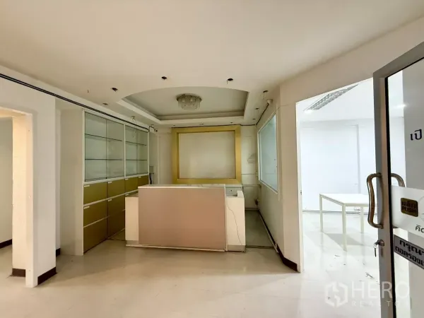 Office Space for rent in Din Daeng, Bangkok - Reception area with front desk, built-in glass cabinets and a glass entry door in neutral tones.