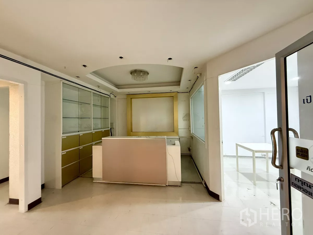 Office Space for rent in Din Daeng, Bangkok - Reception area with front desk, built-in glass cabinets and a glass entry door in neutral tones.