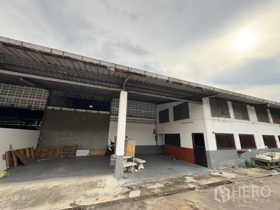 Warehouse for rent in Mueang Samut Prakan, Samut Prakan - Covered loading bay and two-storey office facade of a warehouse in Mueang Samut Prakan with concrete driveway.