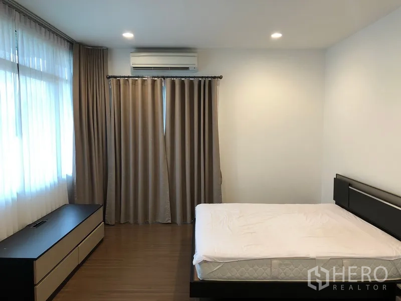 Detached House for rent or sale in Bang Kapi, Bangkok - Large bedroom with bed, air conditioner, blackout drapes and a low media console.