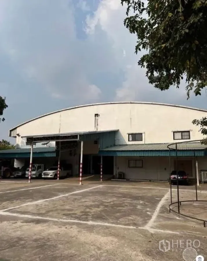 Warehouse for sale in Bang Bua Thong, Nonthaburi - Front elevation of the warehouse with canopy parking and spacious concrete forecourt.