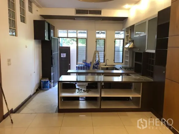 Townhouse for rent or sale in Watthana, Bangkok - Spacious kitchen with an island counter, built-in cabinetry and large windows, shown during light renovation.