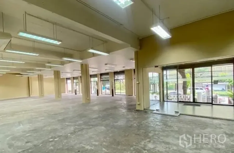 Office Space for rent in Chatuchak, Bangkok - Spacious open-plan office for rent in Chatuchak with large glass frontage, high ceilings, suspended fluorescent lighting and bare concrete floors.