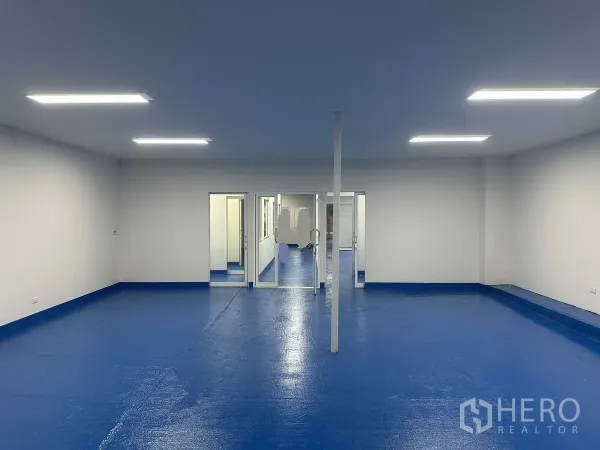 货栈 出租在Pak Kret, Nonthaburi - 宽敞开放空间，蓝色卫生地坪与通向控制间的玻璃门。
