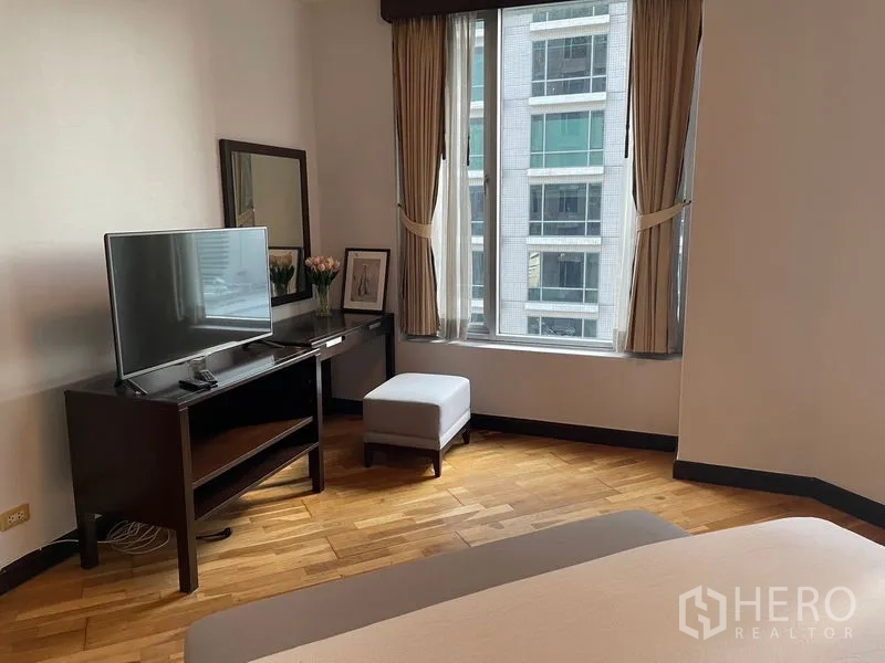 Condominium for rent in Pathum Wan, Bangkok - Bedroom corner with TV stand, mirror, ottoman and large window overlooking city.