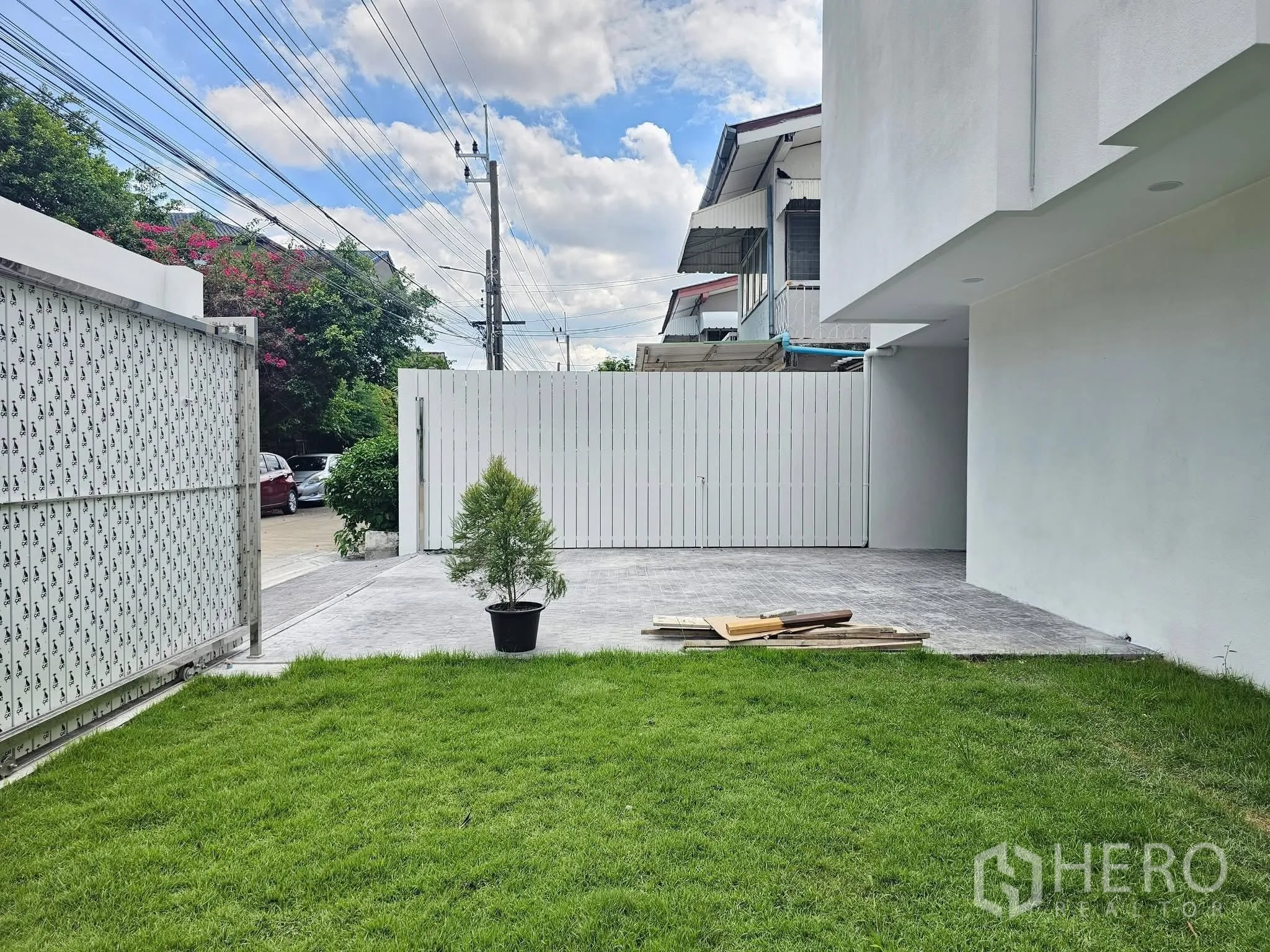 Detached House for sale in Lat Phrao, Bangkok - Front yard with green lawn and paved driveway behind a secure sliding gate.