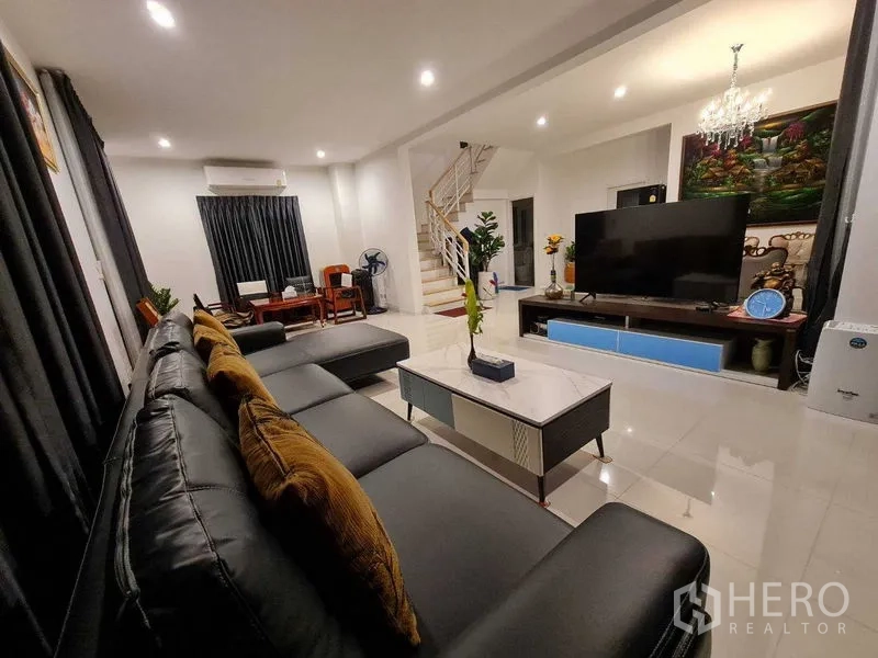 Detached House for rent or sale in Pathum Thani - Spacious lounge with L-shaped leather sofa, marble coffee table, media console and staircase in a Pathum Thani family home.