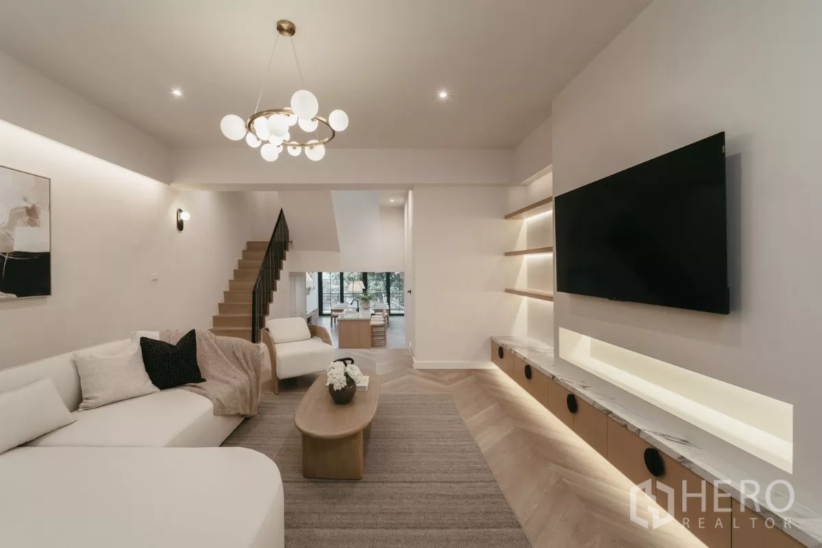 Townhouse for rent in Watthana, Bangkok - Living area facing staircase and TV wall with warm lighting and wood floors.
