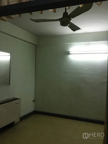 Shophouse for rent in Phra Khanong, Bangkok - Small room with ceiling fan, fluorescent lighting, and wall mirror.