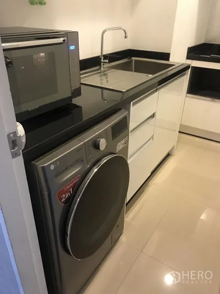 Condominium for rent or sale in Huai Khwang, Bangkok - Compact kitchen with black countertops, sink, microwave and LG washer–dryer combo.