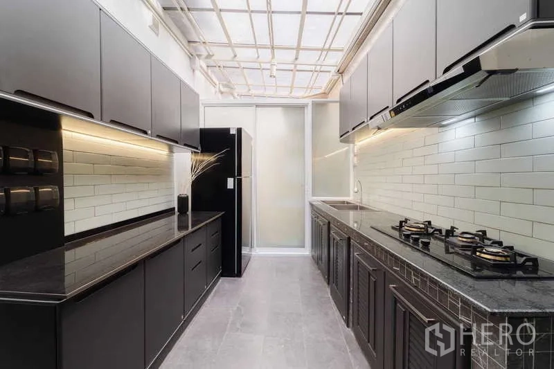 Townhouse for rent or sale in Watthana, Bangkok - Thai kitchen with black cabinets, gas hobs, and subway-tile backsplash.