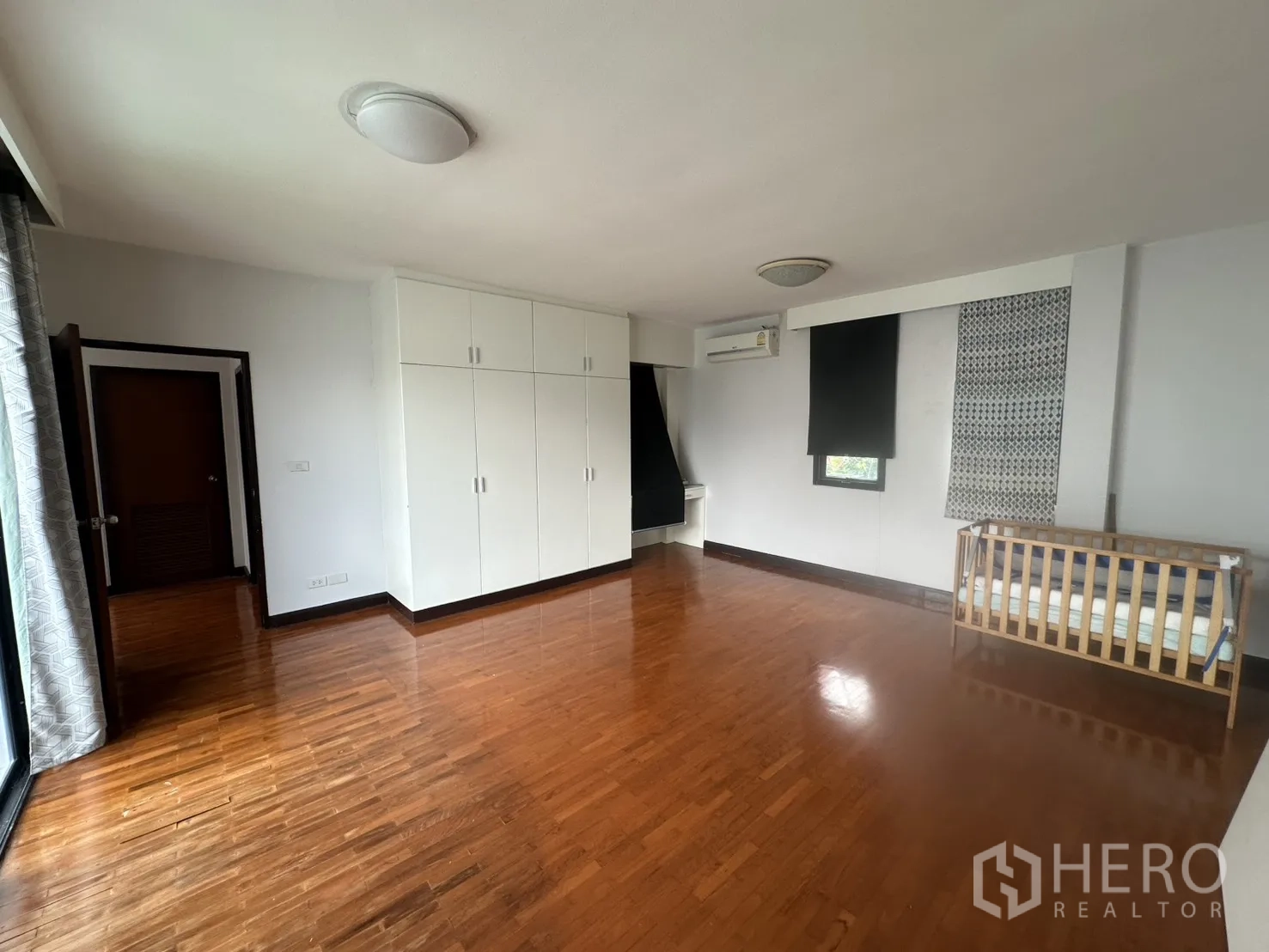 Detached House for rent in Watthana, Bangkok - Bedroom with built-in white wardrobes, wood floors, and crib.