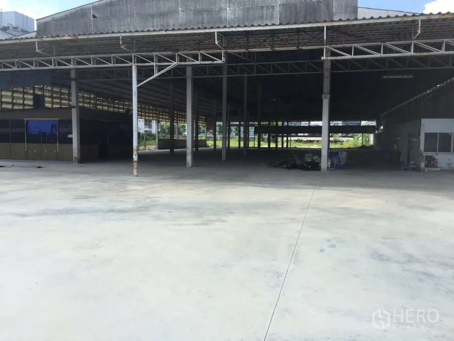 Warehouse for rent in Khlong Luang, Pathum Thani - Open warehouse interior in Khlong Luang with high steel truss roof, concrete floor, and a large covered loading area.