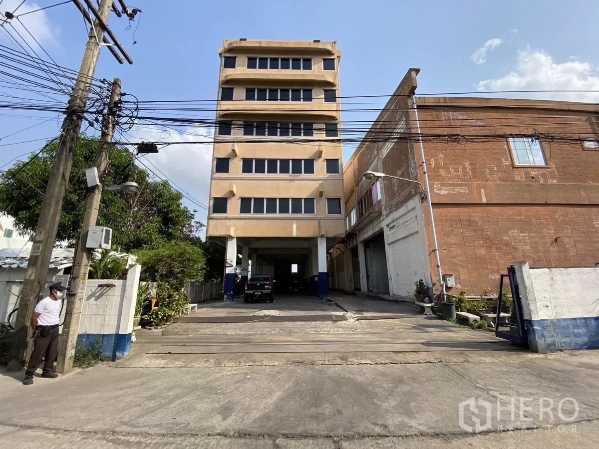 工厂 出售在Bang Phli, Samut Prakan - 街景：六层办公楼与工厂相连，下方有车道通行。
