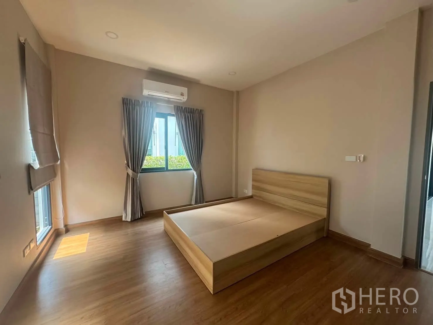 Detached House for rent or sale in Prawet, Bangkok - Bright bedroom with wood floors, a wooden bed frame, curtains, and an air conditioner.