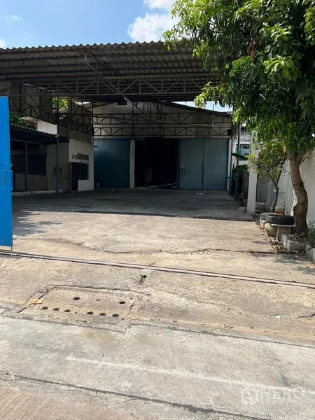 货栈 出租在Khlong Toei, Bangkok - 带大门的仓库入口，宽阔混凝土车道与高金属屋顶。