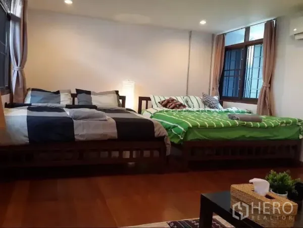 Townhouse for rent in Khlong Toei, Bangkok - Spacious bedroom with two double beds, wood flooring, large curtained windows, and warm ambient lights.