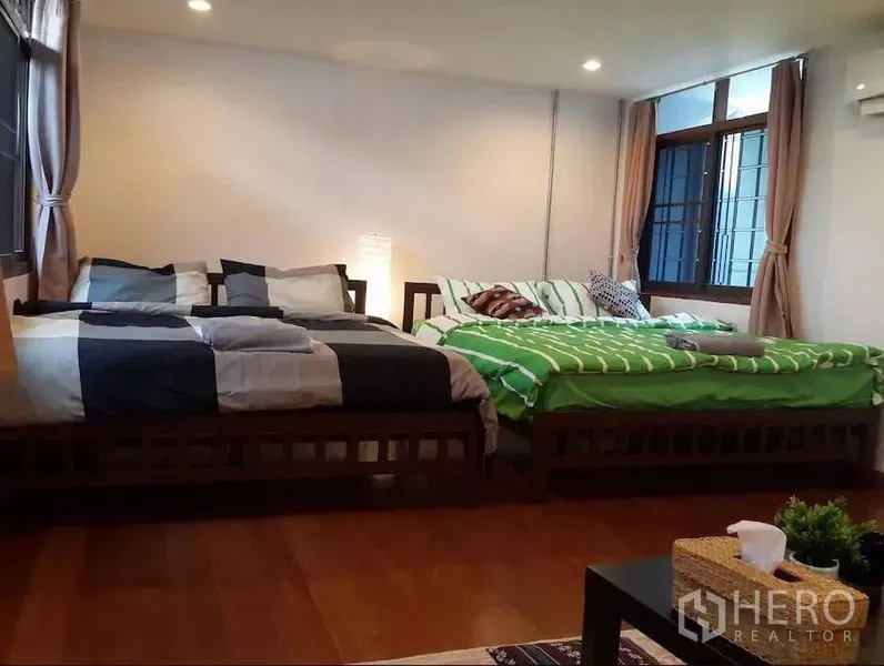 Townhouse for rent in Khlong Toei, Bangkok - Spacious bedroom with two double beds, wood flooring, large curtained windows, and warm ambient lights.