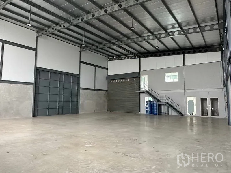 Warehouse for rent in Samut Prakan - Warehouse hall showing large sliding door, roller shutter and mezzanine office with stairs.