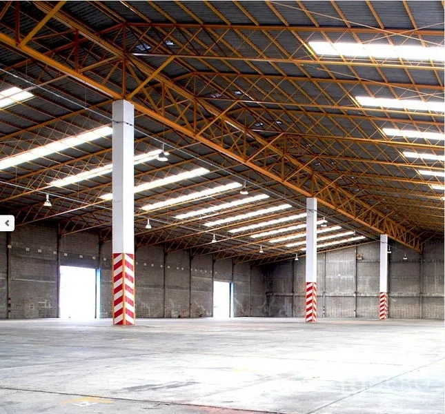 Factory for rent in Samut Prakan - Expansive warehouse interior with high steel truss roof, skylights, concrete floor, and multiple loading bays.
