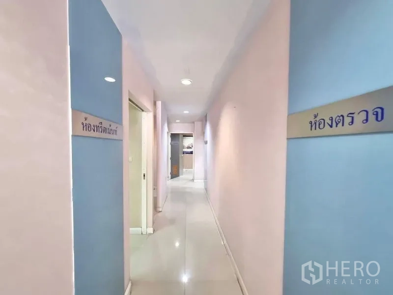 Shophouse for rent in Watthana, Bangkok - Long interior corridor with Thai room signs and glossy tiled floor.