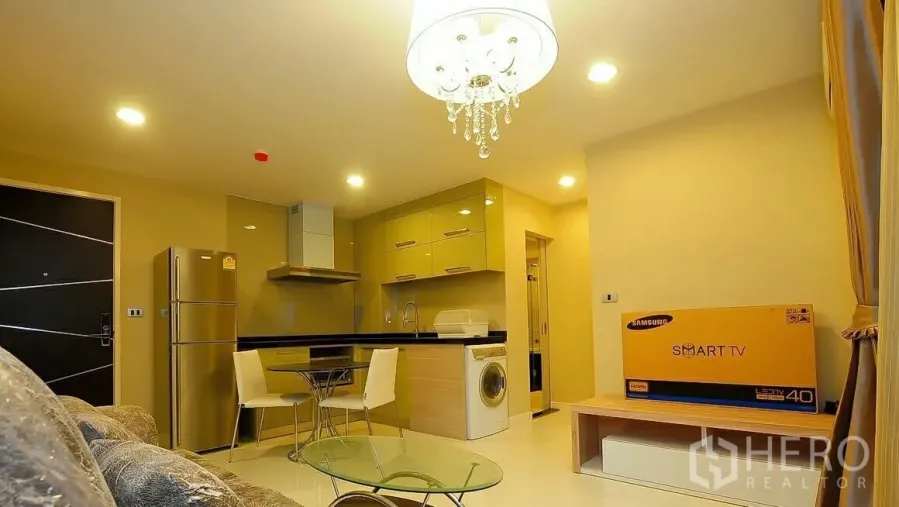 Condominium for sale in Khlong Toei, Bangkok - Open-plan living and kitchen with chandelier, stainless fridge, washing machine, and boxed TV in a Sukhumvit condo.