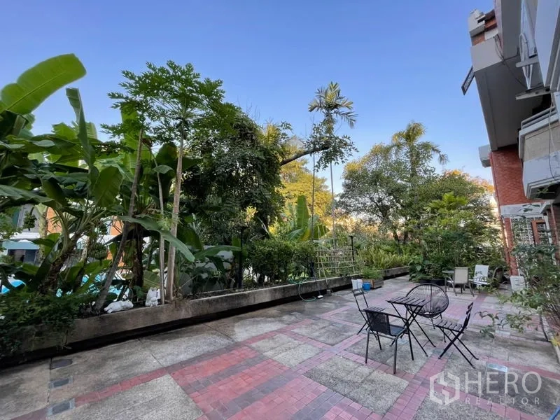 联排别墅 出租在Khlong Toei, Bangkok - 宽阔铺砖露台配户外桌椅，旁有郁郁葱葱的热带花园。