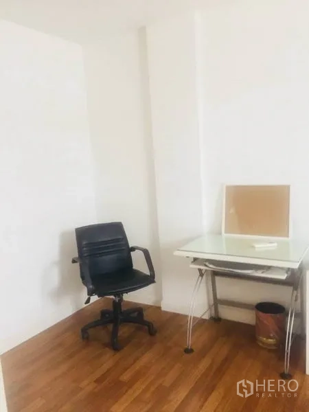 联排别墅 出租在Bang Kapi, Bangkok - 明亮书房角，白墙、玻璃桌与黑色办公椅，木地板。