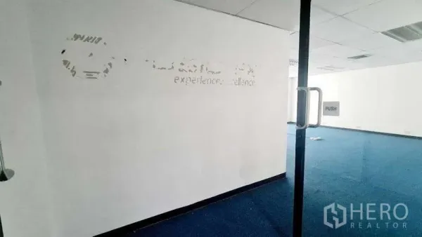 Office Space for rent in Khlong Toei, Bangkok - Open-plan office with blue carpet and drop ceiling viewed through a clear glass door.