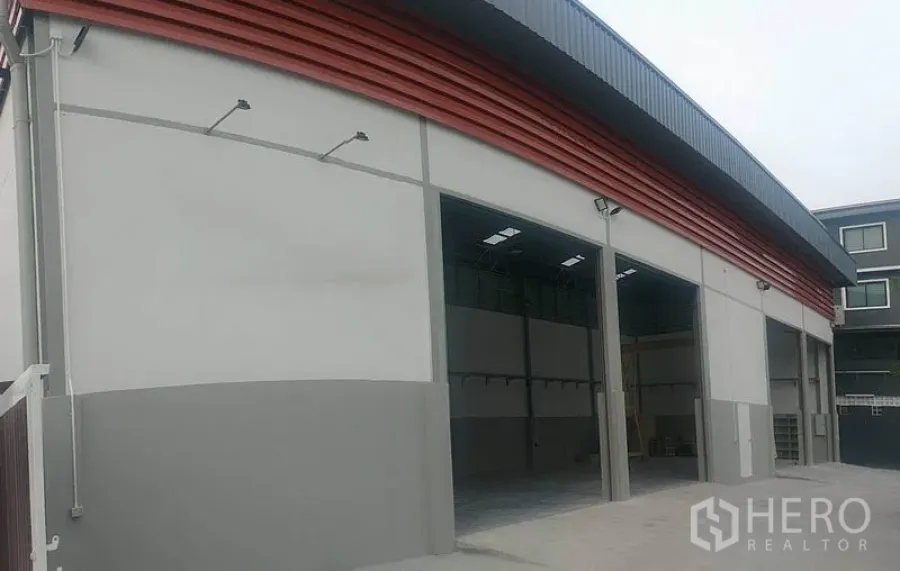 货栈 出租在Saphan Sung, Bangkok - 现代仓库外立面，大型卷闸门与红色装饰板。