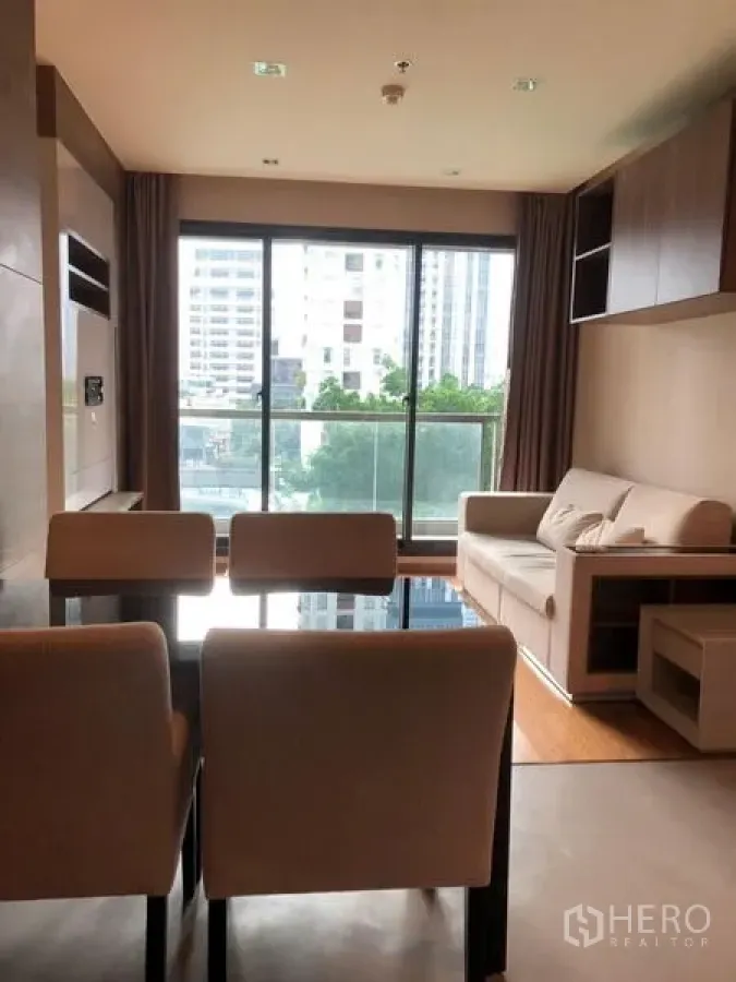 Condominium for sale in Bang Rak, Bangkok - Bright living and dining area with sofa, dining chairs and floor-to-ceiling windows with city view.
