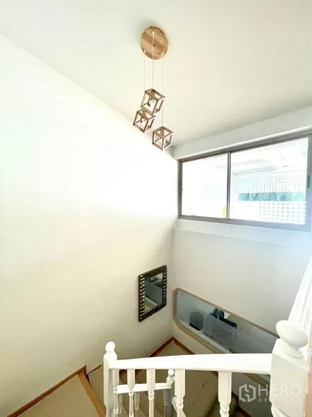 Townhouse for rent in Khlong Toei, Bangkok - Stairwell with large window, white railing and trio of cube pendant lights.