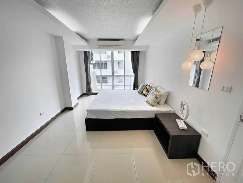 Condominium for rent in Khlong Toei, Bangkok - Spacious master bedroom with bed, pendant lights and sliding glass doors to a balcony.