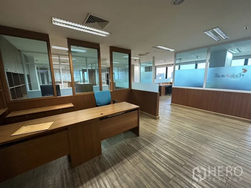 Office Space for rent or sale - Work area with glass partitions, wooden desks and overhead fluorescent lights.