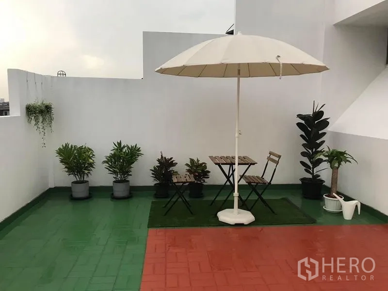 Townhouse for sale in Suan Luang, Bangkok - Rooftop patio with white umbrella, bistro set and potted greenery.