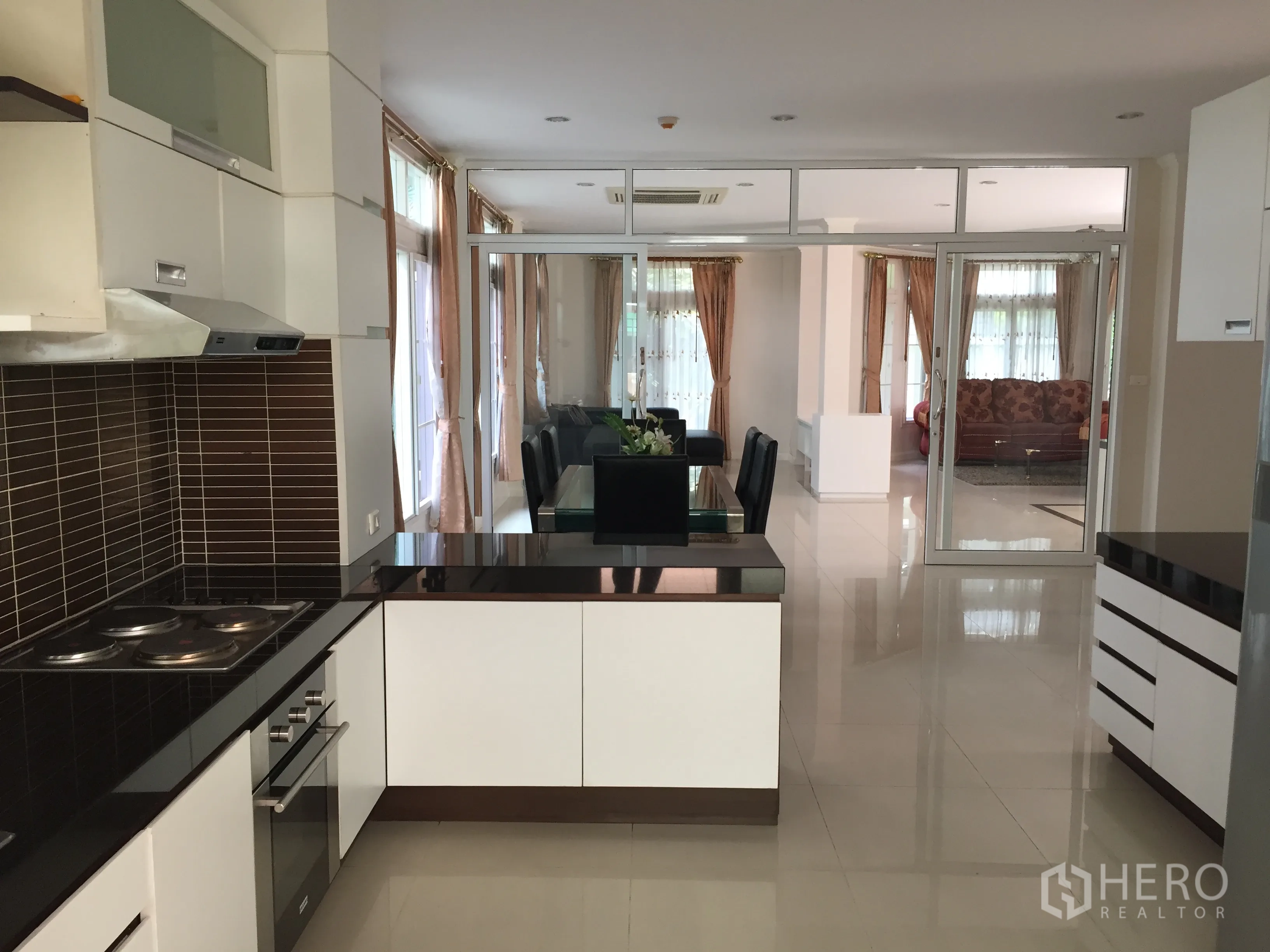 Detached House for rent or sale in Lat Phrao, Bangkok - Modern open kitchen facing dining and living areas with glossy countertops and ample storage.